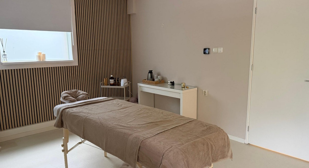 De behandelruimte met massagetafel, houten lattenwand en een klein raam