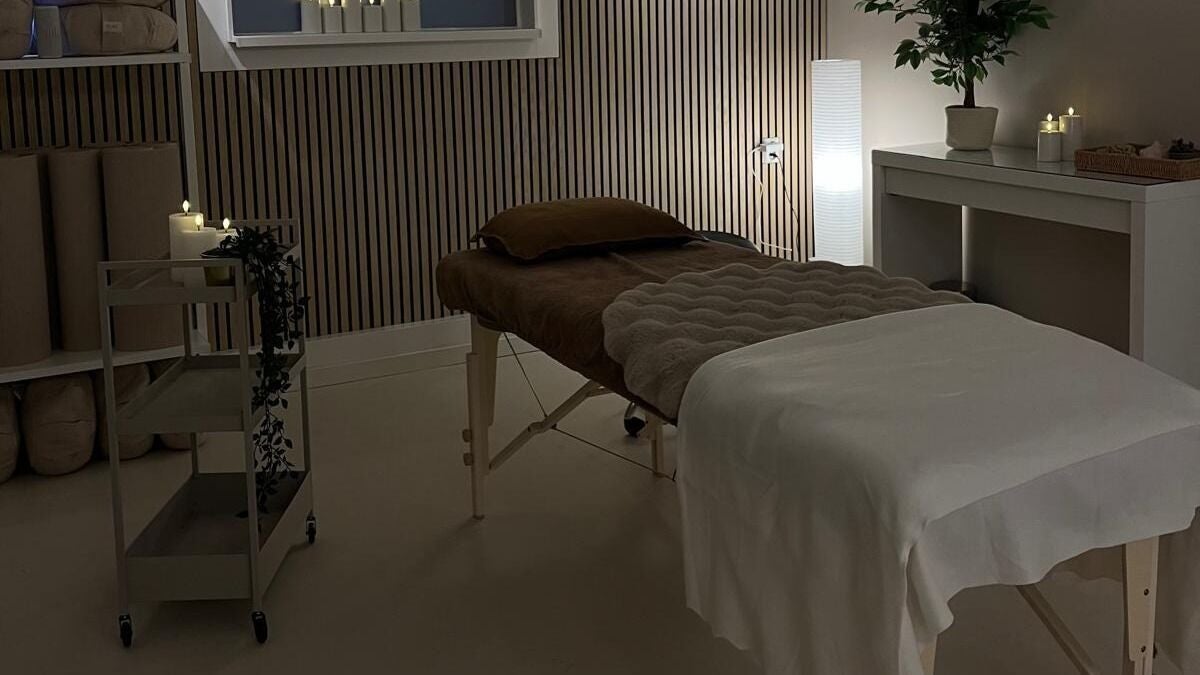 De massagetafel bij gedimd licht, met kaarsen en een plant op de kast